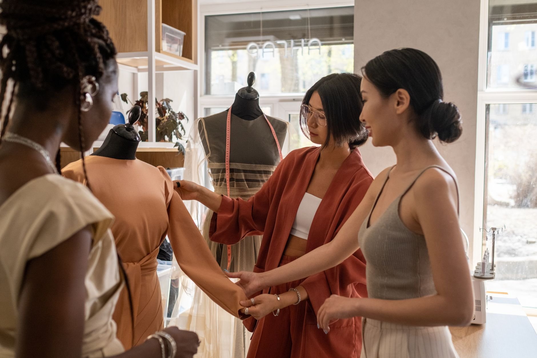 Three women collaborate in a fashion studio, designing and discussing elegant dresses